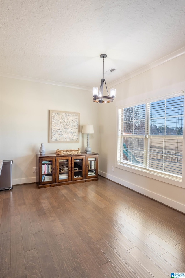 unfurnished living room featuring ornamental molding, hardwood / wood-style flooring, an inviting chandelier, and a textured ceiling