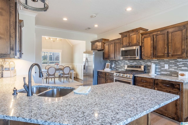 kitchen with sink, light stone counters, ornamental molding, and stainless steel appliances