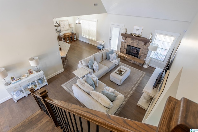 living room with dark wood-type flooring, high vaulted ceiling, and a stone fireplace