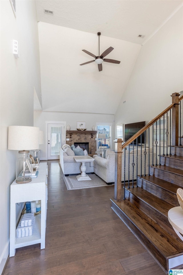 living room featuring ceiling fan, dark hardwood / wood-style flooring, high vaulted ceiling, and a stone fireplace