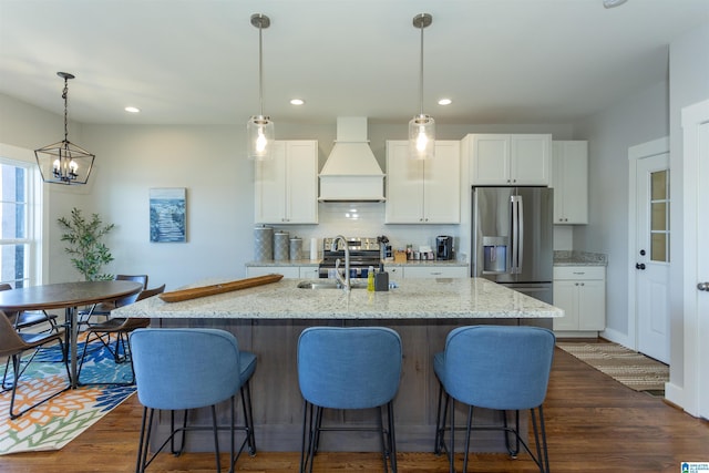 kitchen featuring premium range hood, sink, stainless steel fridge with ice dispenser, a center island with sink, and white cabinets