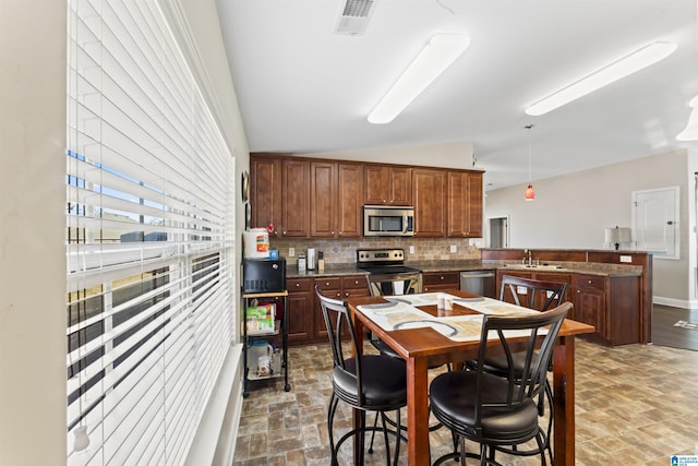 kitchen featuring appliances with stainless steel finishes, lofted ceiling, sink, decorative backsplash, and kitchen peninsula