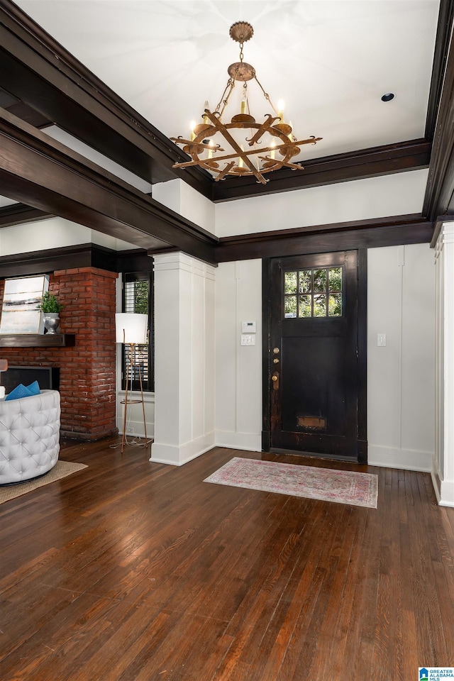 entrance foyer with ornamental molding, a brick fireplace, a chandelier, and dark hardwood / wood-style flooring