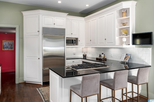 kitchen with dark wood-type flooring, appliances with stainless steel finishes, a kitchen breakfast bar, white cabinets, and kitchen peninsula