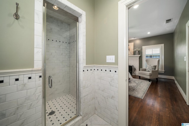 bathroom with wood-type flooring, tile walls, a fireplace, and walk in shower