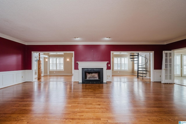 unfurnished living room featuring crown molding, a fireplace, french doors, and light wood-type flooring