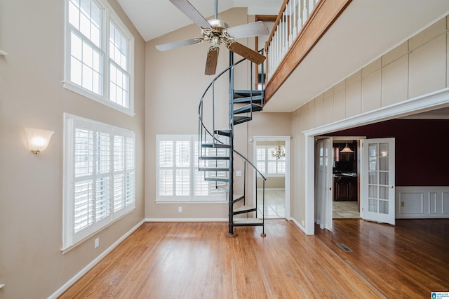 unfurnished living room with ceiling fan, light hardwood / wood-style flooring, and a high ceiling