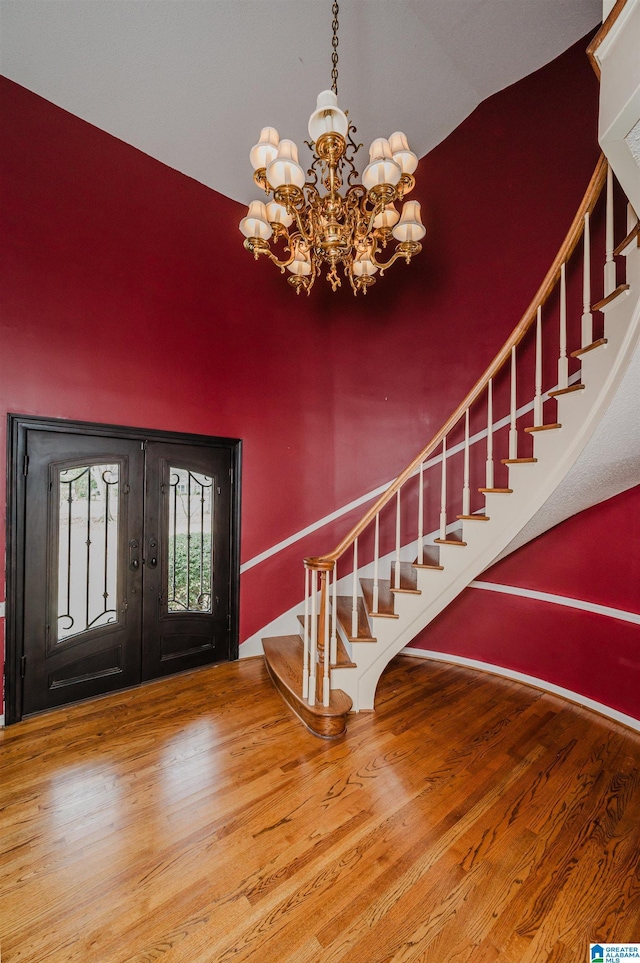 entrance foyer with hardwood / wood-style flooring, vaulted ceiling, a notable chandelier, and french doors