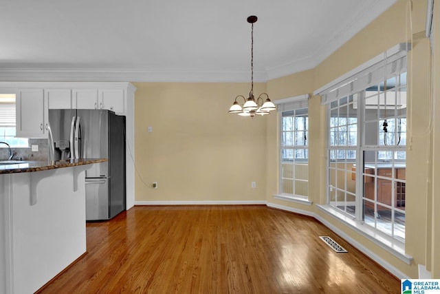 kitchen with stainless steel refrigerator with ice dispenser, hanging light fixtures, ornamental molding, hardwood / wood-style flooring, and white cabinets