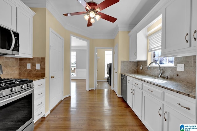 kitchen with sink, white cabinetry, dark stone countertops, ornamental molding, and appliances with stainless steel finishes