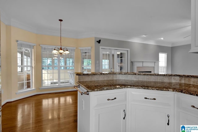 kitchen with white cabinetry, ornamental molding, dark stone counters, and hanging light fixtures