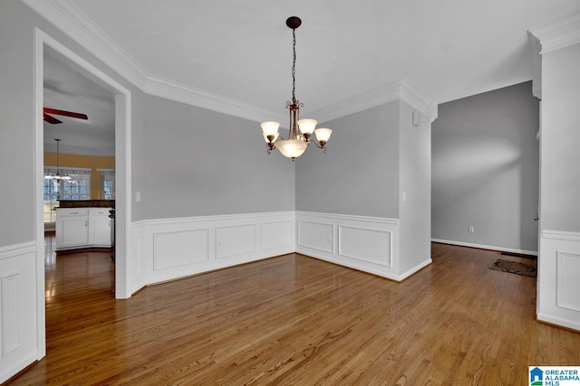 unfurnished dining area featuring wood-type flooring, ornamental molding, and ceiling fan with notable chandelier