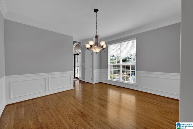 unfurnished dining area with wood-type flooring, crown molding, and a chandelier