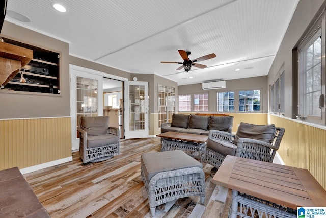 living room with ceiling fan, wooden walls, light wood-type flooring, and an AC wall unit