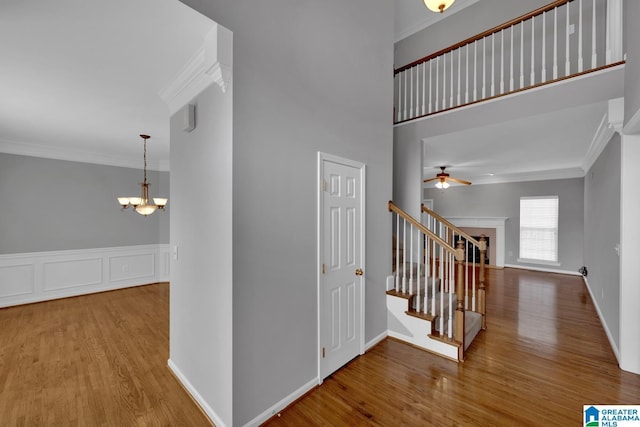 stairs featuring crown molding, wood-type flooring, ceiling fan with notable chandelier, and a high ceiling