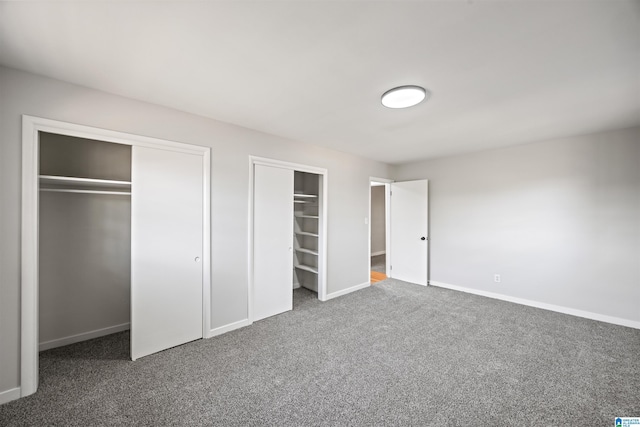 unfurnished bedroom with dark colored carpet and two closets