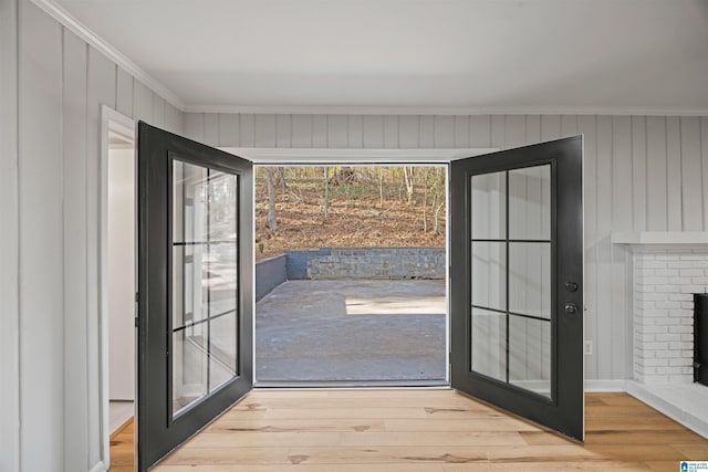 doorway to outside featuring crown molding, a brick fireplace, and light hardwood / wood-style flooring