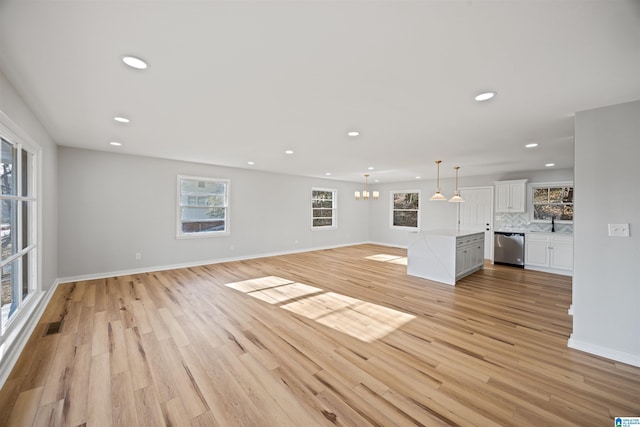 unfurnished living room with sink, an inviting chandelier, and light wood-type flooring