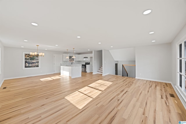 unfurnished living room featuring a chandelier, vaulted ceiling, and light hardwood / wood-style flooring