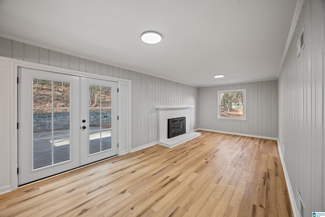 unfurnished living room with a brick fireplace, ornamental molding, light hardwood / wood-style floors, and french doors