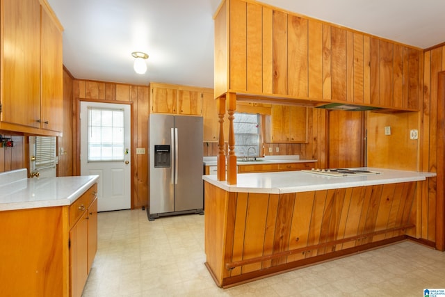 kitchen featuring sink, stainless steel fridge with ice dispenser, white gas stovetop, wooden walls, and kitchen peninsula