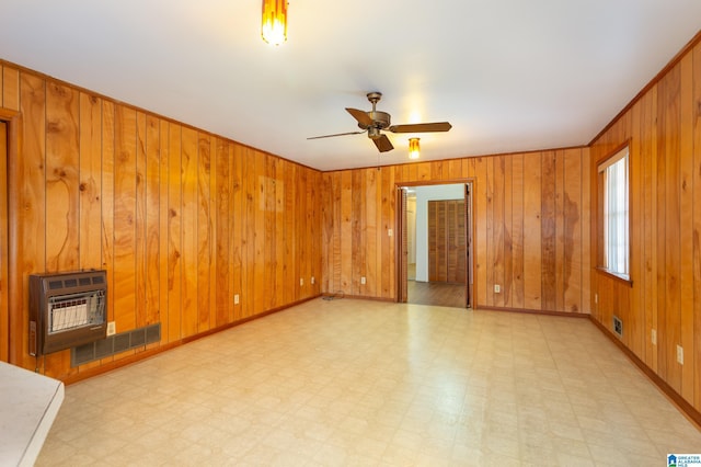 empty room featuring ceiling fan, wooden walls, and heating unit