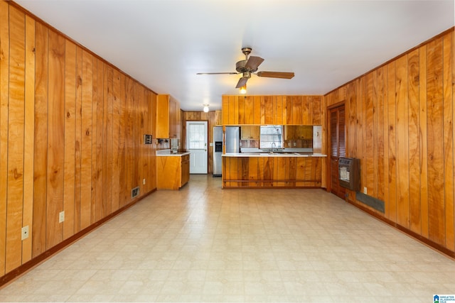 kitchen featuring heating unit, stainless steel fridge with ice dispenser, wooden walls, kitchen peninsula, and ceiling fan