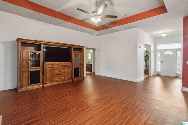 unfurnished living room with dark wood-type flooring, a raised ceiling, and ceiling fan