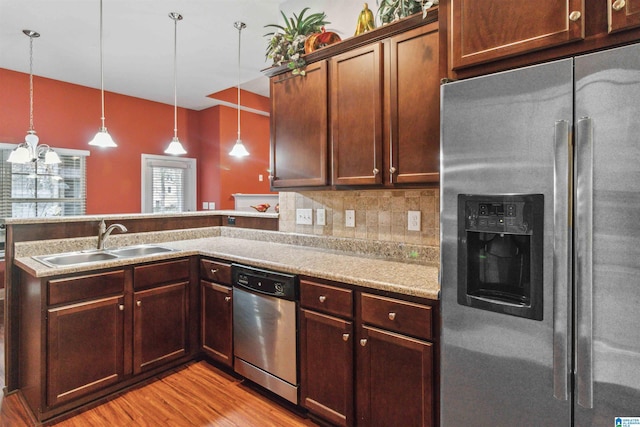 kitchen featuring sink, light hardwood / wood-style flooring, appliances with stainless steel finishes, tasteful backsplash, and decorative light fixtures