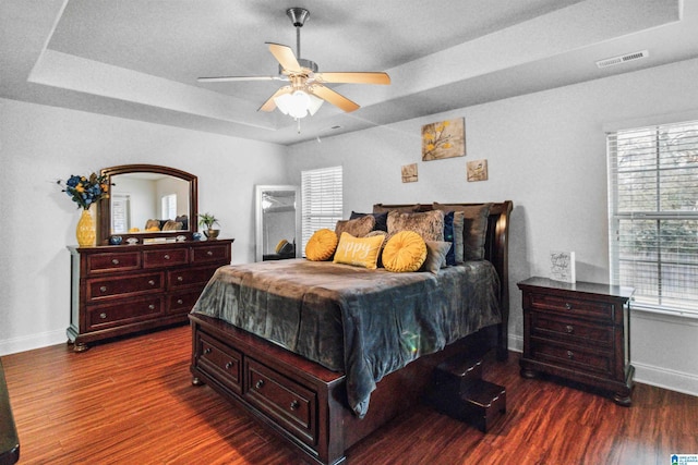 bedroom with dark hardwood / wood-style floors, a raised ceiling, and ceiling fan