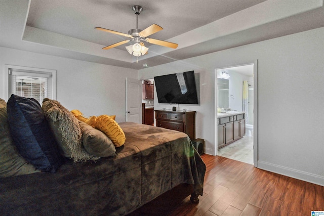 bedroom with light hardwood / wood-style floors, a raised ceiling, ceiling fan, and ensuite bathroom