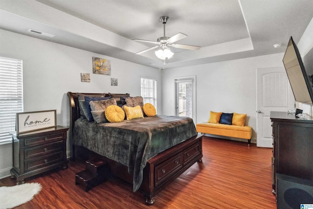 bedroom featuring a raised ceiling, dark wood-type flooring, and ceiling fan