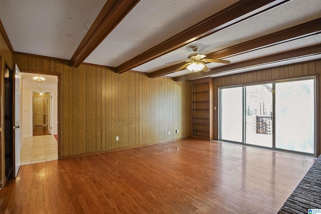 empty room featuring wooden walls, a textured ceiling, beam ceiling, and light hardwood / wood-style flooring