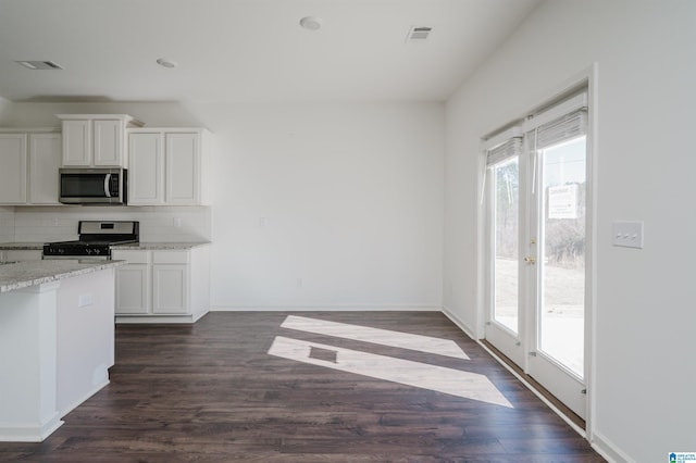 kitchen featuring dark wood-type flooring, appliances with stainless steel finishes, white cabinetry, backsplash, and light stone counters