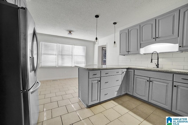 kitchen with gray cabinetry, light tile patterned floors, stainless steel fridge, kitchen peninsula, and decorative backsplash