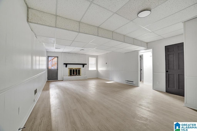 unfurnished living room featuring a baseboard heating unit, a drop ceiling, a fireplace, and light hardwood / wood-style flooring