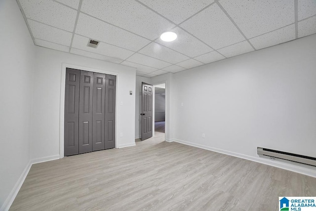 unfurnished bedroom with baseboard heating, light hardwood / wood-style floors, a closet, and a drop ceiling