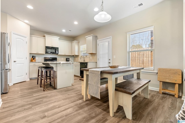 kitchen featuring hanging light fixtures, a kitchen island, black appliances, white cabinets, and a kitchen bar