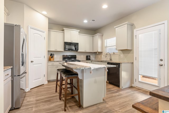 kitchen featuring white cabinetry, light stone counters, a kitchen island, light hardwood / wood-style floors, and black appliances