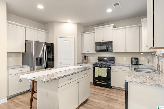 kitchen with sink, white cabinetry, light hardwood / wood-style flooring, a kitchen island, and black appliances