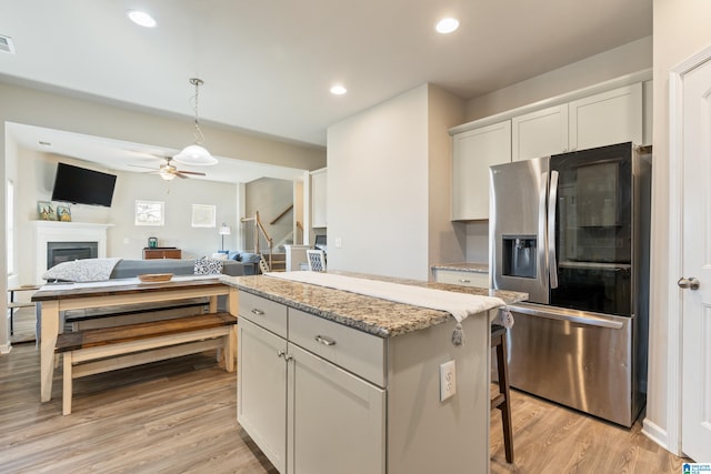 kitchen featuring stainless steel refrigerator with ice dispenser, light wood-type flooring, a kitchen island, pendant lighting, and white cabinets