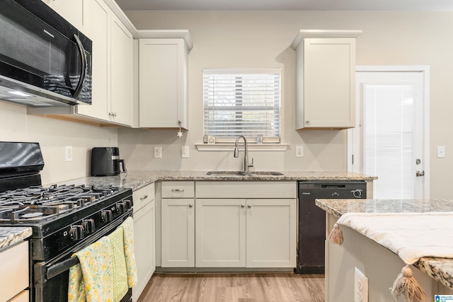 kitchen with sink, white cabinetry, black appliances, light hardwood / wood-style floors, and light stone countertops