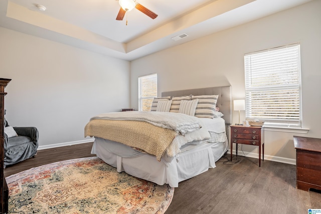 bedroom featuring dark hardwood / wood-style flooring, a tray ceiling, and ceiling fan