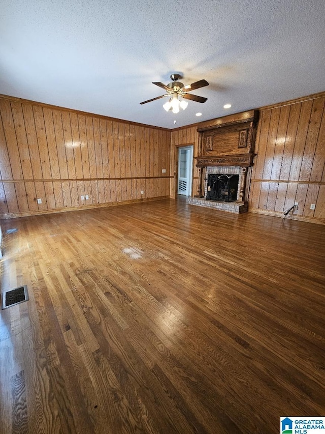 unfurnished living room with ceiling fan, wooden walls, hardwood / wood-style floors, and a textured ceiling