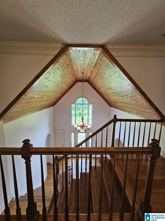 stairs featuring vaulted ceiling, ornamental molding, a textured ceiling, and a chandelier