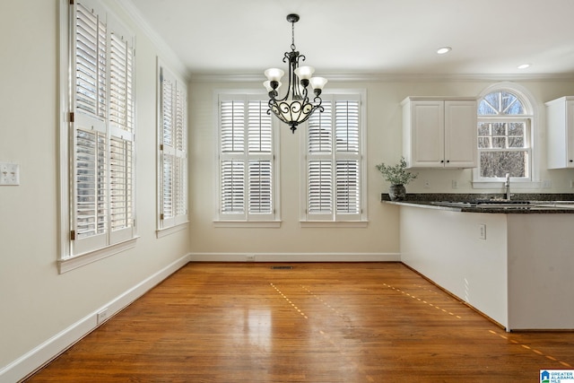 unfurnished dining area featuring ornamental molding, sink, hardwood / wood-style floors, and a chandelier