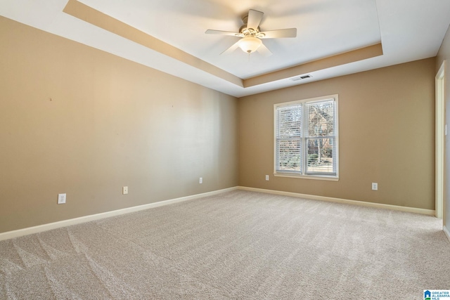 carpeted spare room with a raised ceiling and ceiling fan