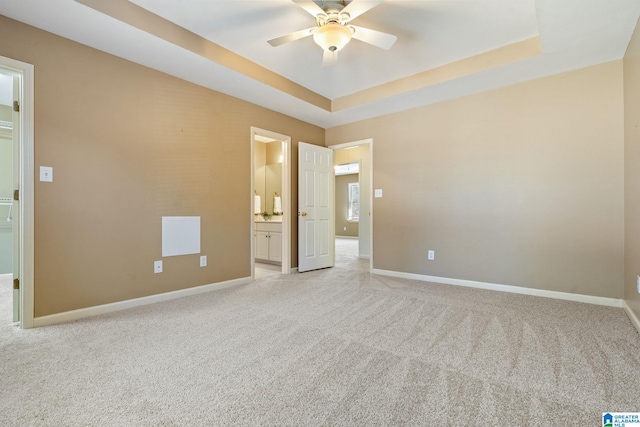 empty room with a raised ceiling, light carpet, and ceiling fan