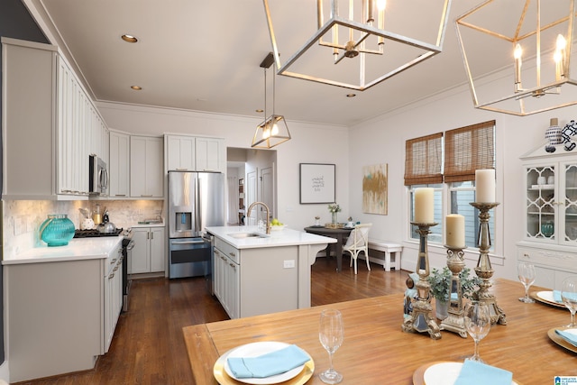 kitchen with sink, hanging light fixtures, appliances with stainless steel finishes, an island with sink, and backsplash