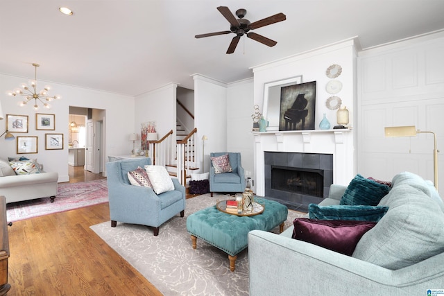 living room with ceiling fan with notable chandelier, ornamental molding, a tiled fireplace, and hardwood / wood-style floors